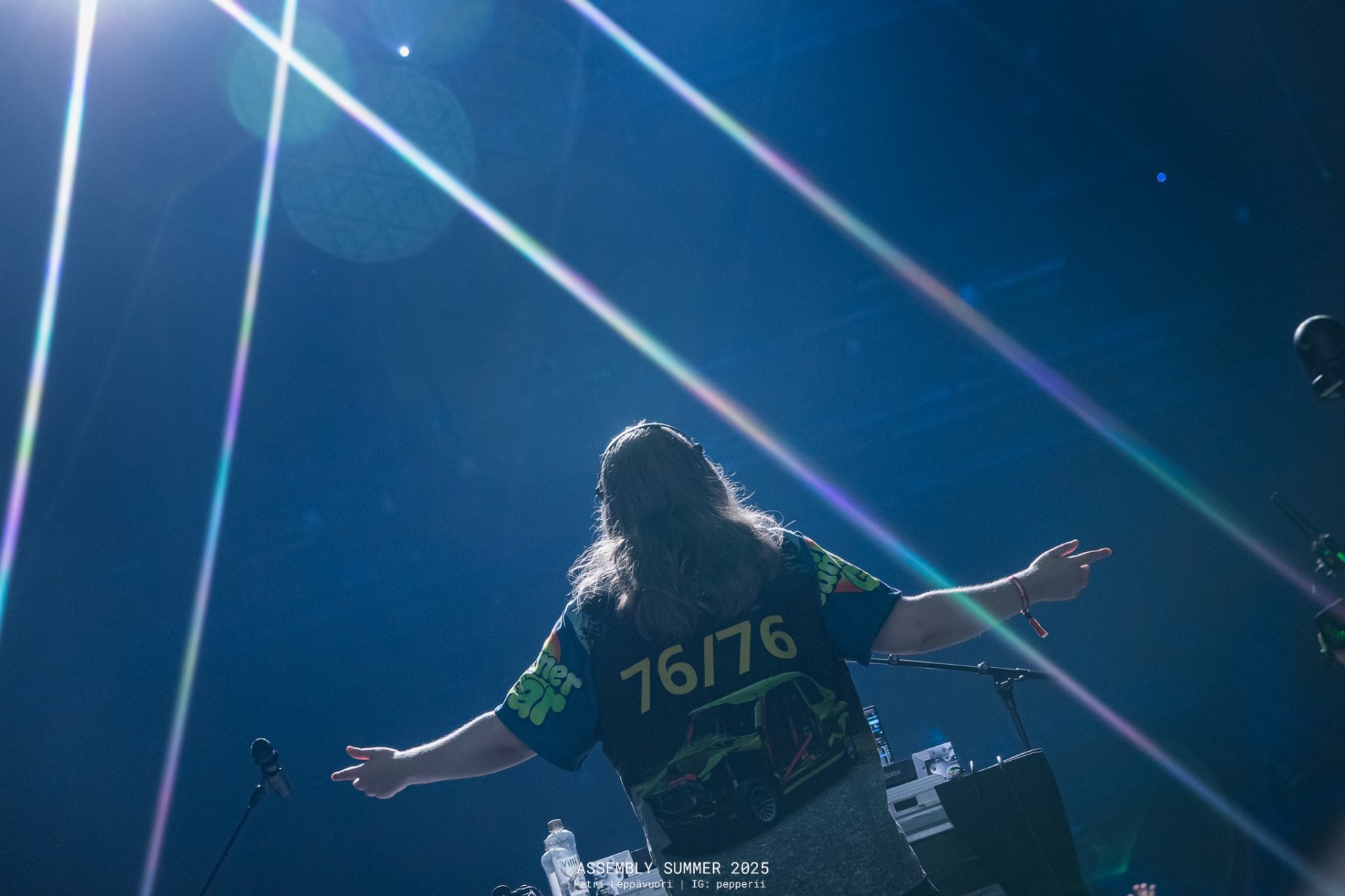 Silhouetted figure with arms outstretched under sweeping blue laser beams at Assembly